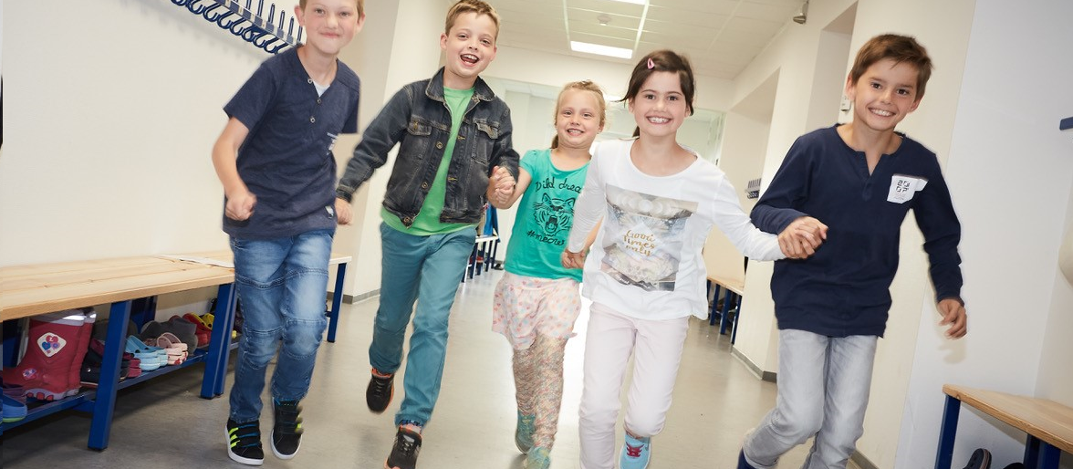 Fünf lachende Grundschulkinder laufen über Schulflur